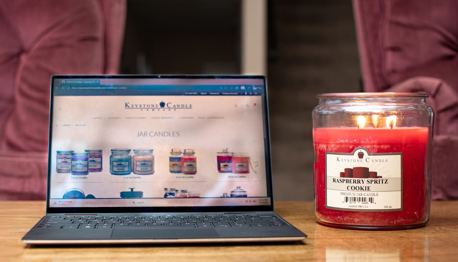 Lit candle next to a computer open to Keystone Candle website